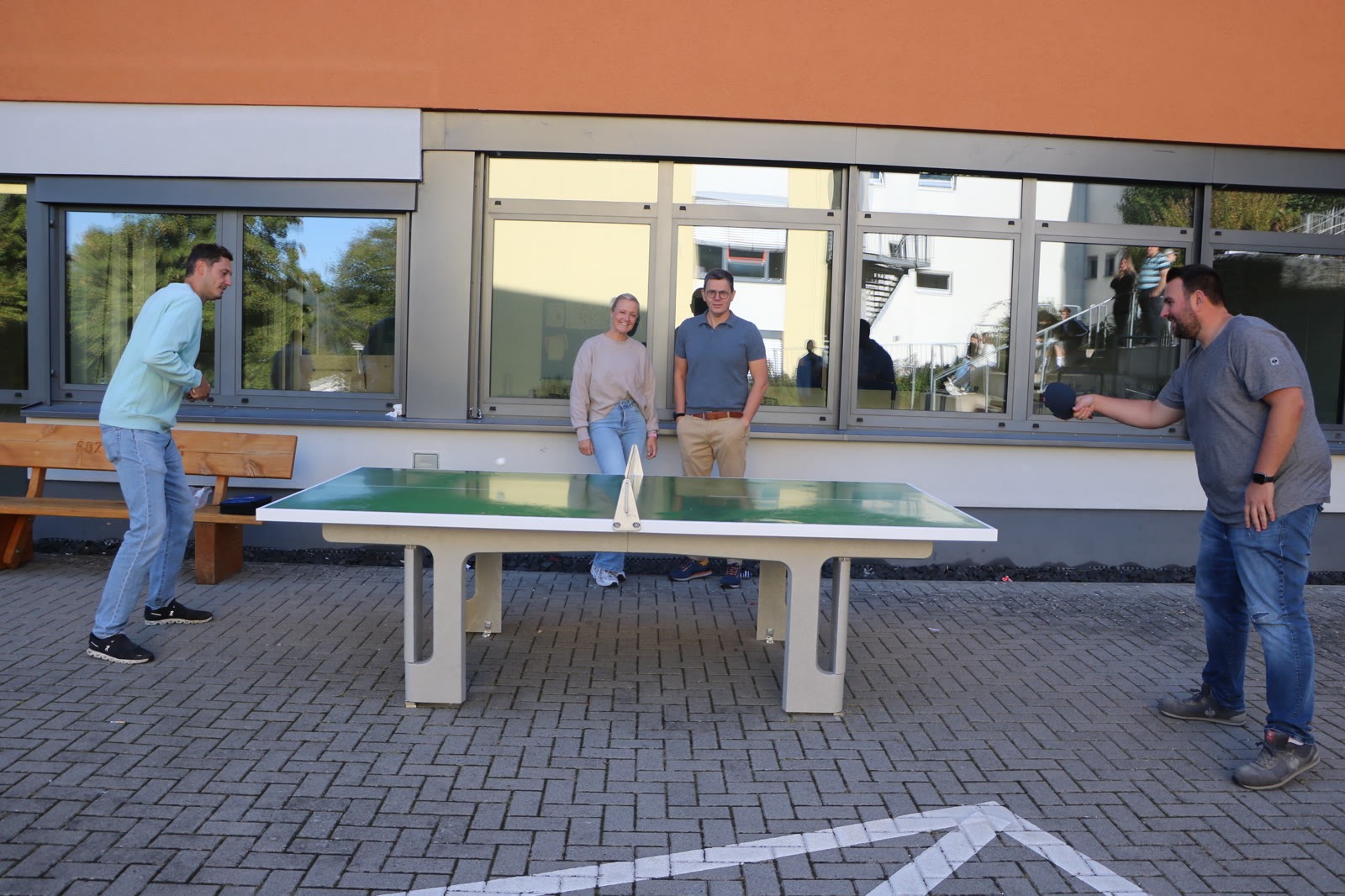 Zwei Lehrkräfte spielen an der neuen Tischtennisplatte im Außenbereich der Wilhelm-Knapp-Schule Weilburg, während Gäste zusehen.
